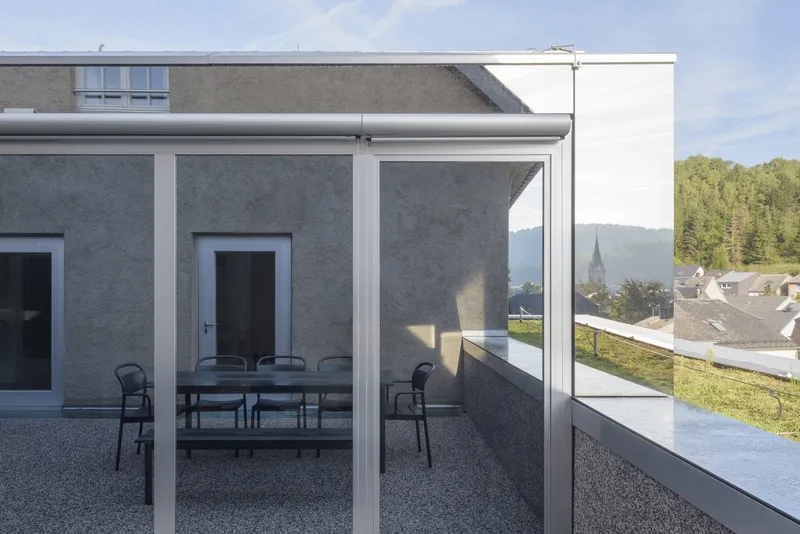 Rooftop terrace with glass balustrade and dining furniture overlooking a church spire and village