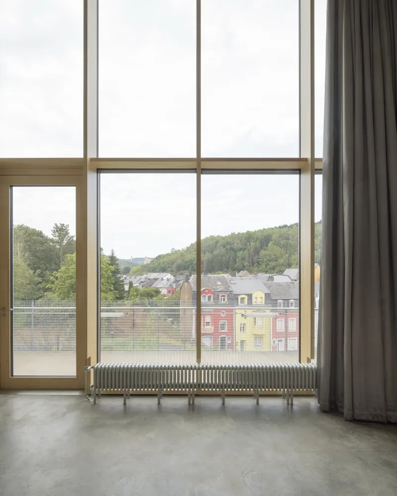 Floor-to-ceiling window with timber frame overlooking residential rooftops and forested hillside