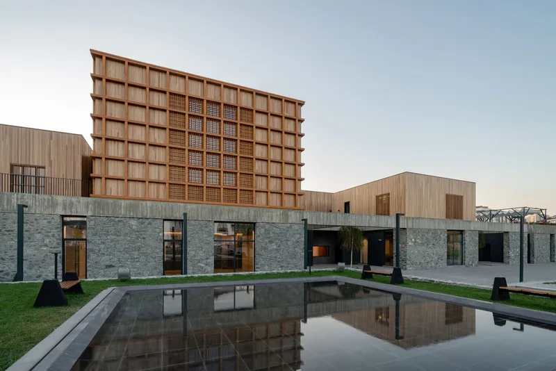 Courtyard reflecting pool with timber grid tower and stone-clad ground floor illuminated at twilight
