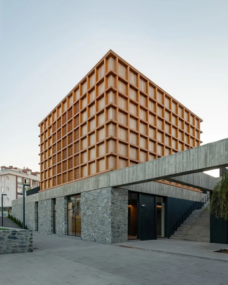 Timber grid facade rising above a stone and concrete base with residential buildings visible in the background