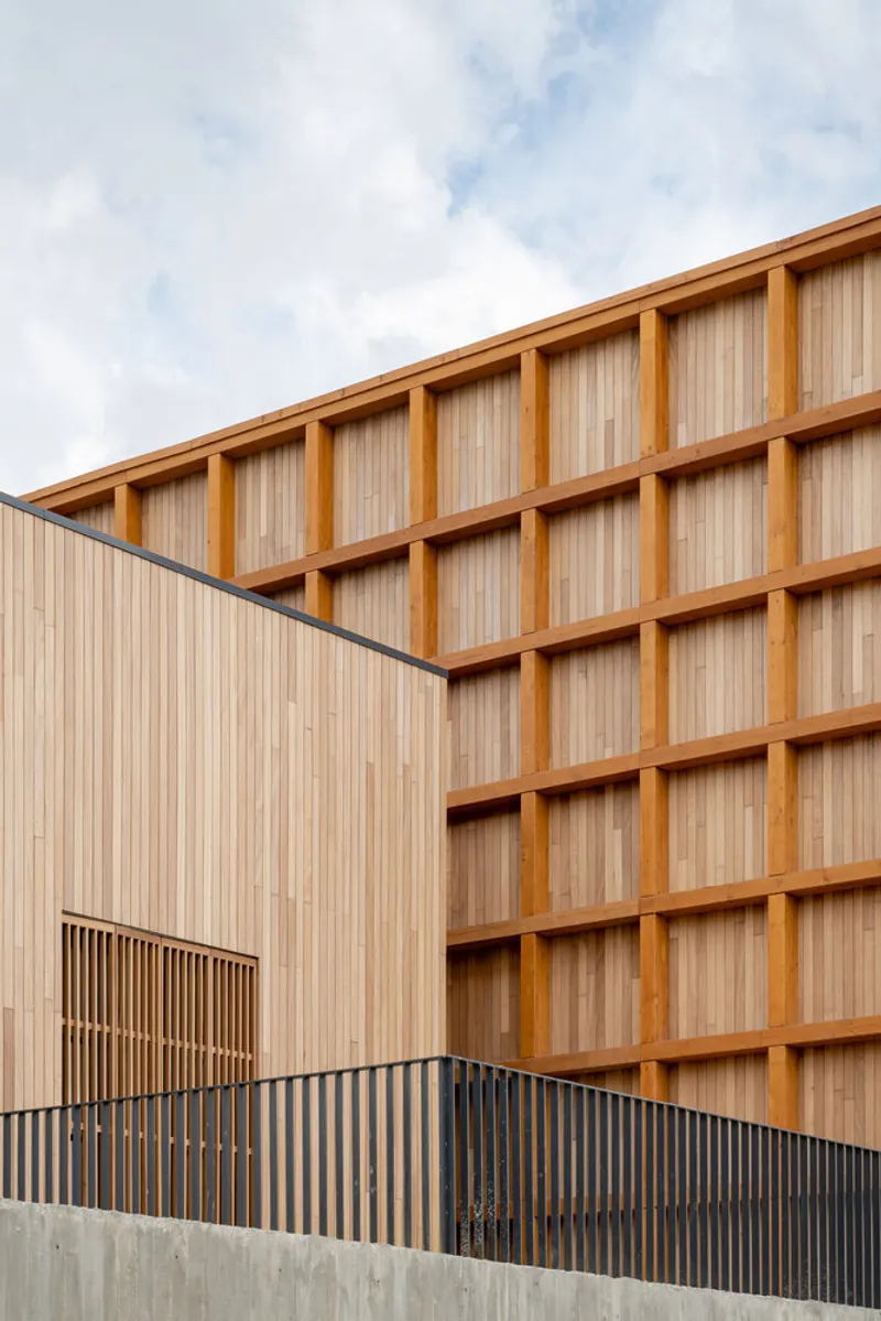Corner detail of vertical timber cladding meeting the exposed grid structure under partly cloudy skies