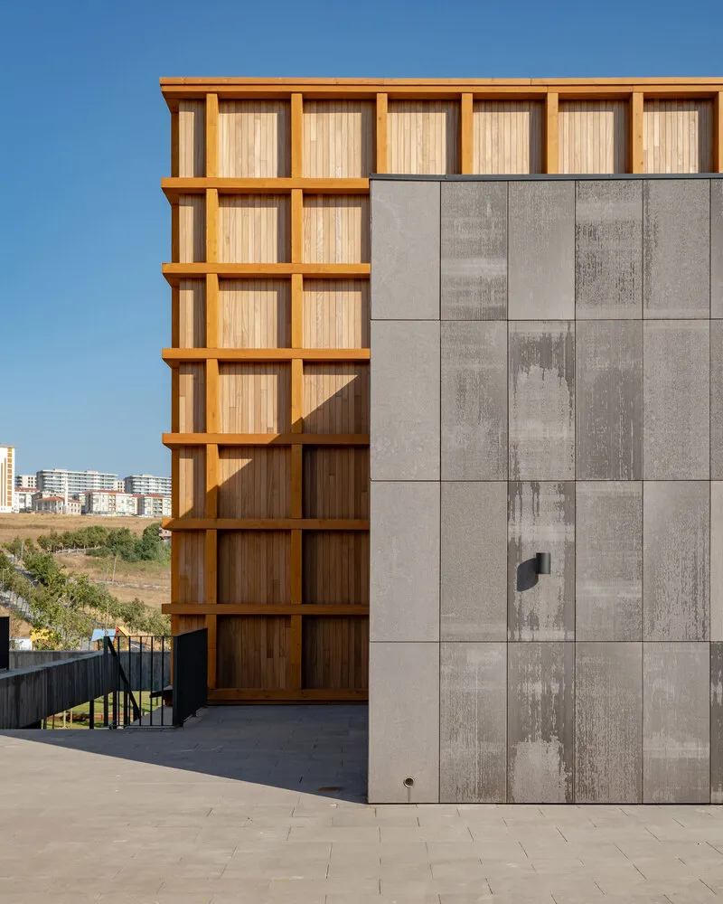 Timber frame tower with grid pattern beside weathered concrete panel wall on paved terrace