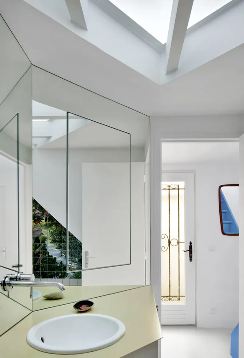 Bathroom with angled mirror above pale yellow sink counter and exposed ceiling beams in daylight