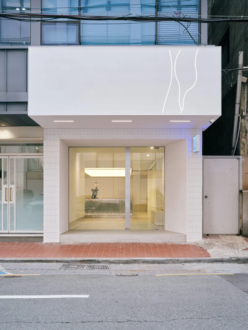 Street view of the white tiled storefront with recessed entrance and illuminated interior