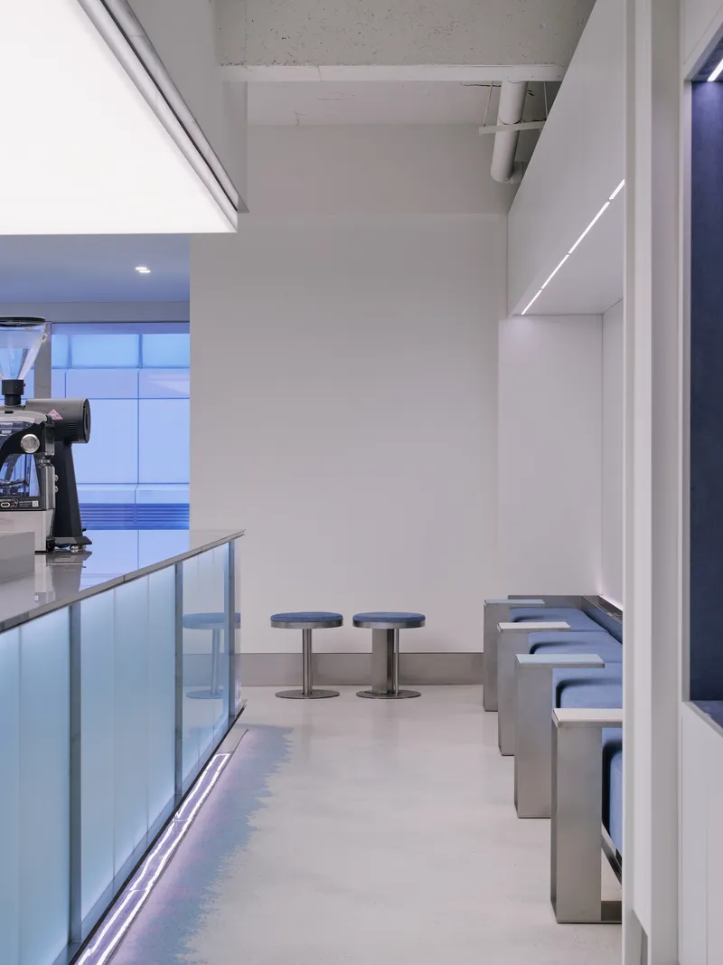 Seating area with metal stools and banquette along white paneled walls under exposed concrete ceiling