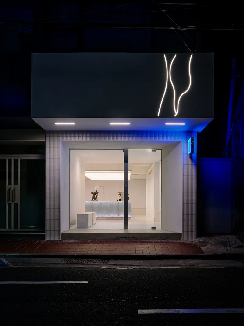 Street facade with illuminated signage and glass storefront framed by white tile at night