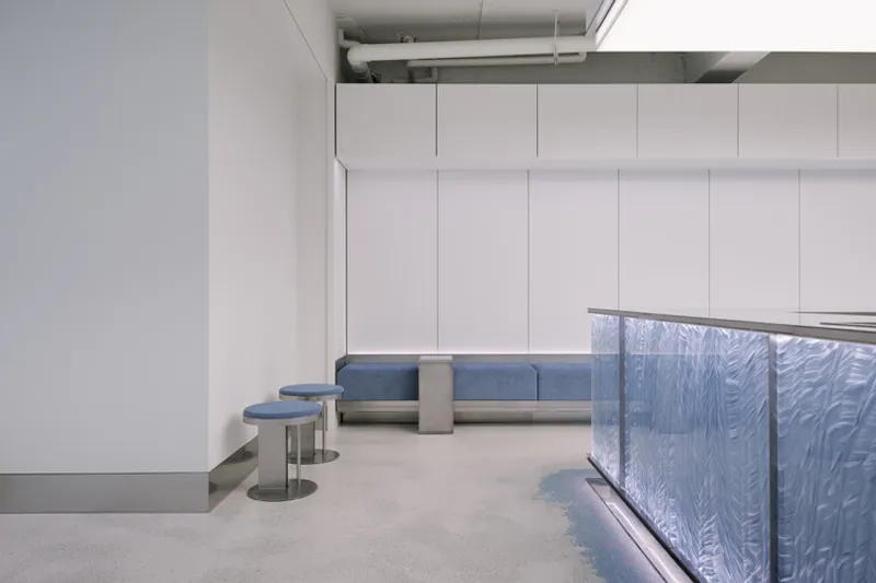 Corner view showing blue upholstered bench beside iridescent paneled counter with recessed lighting
