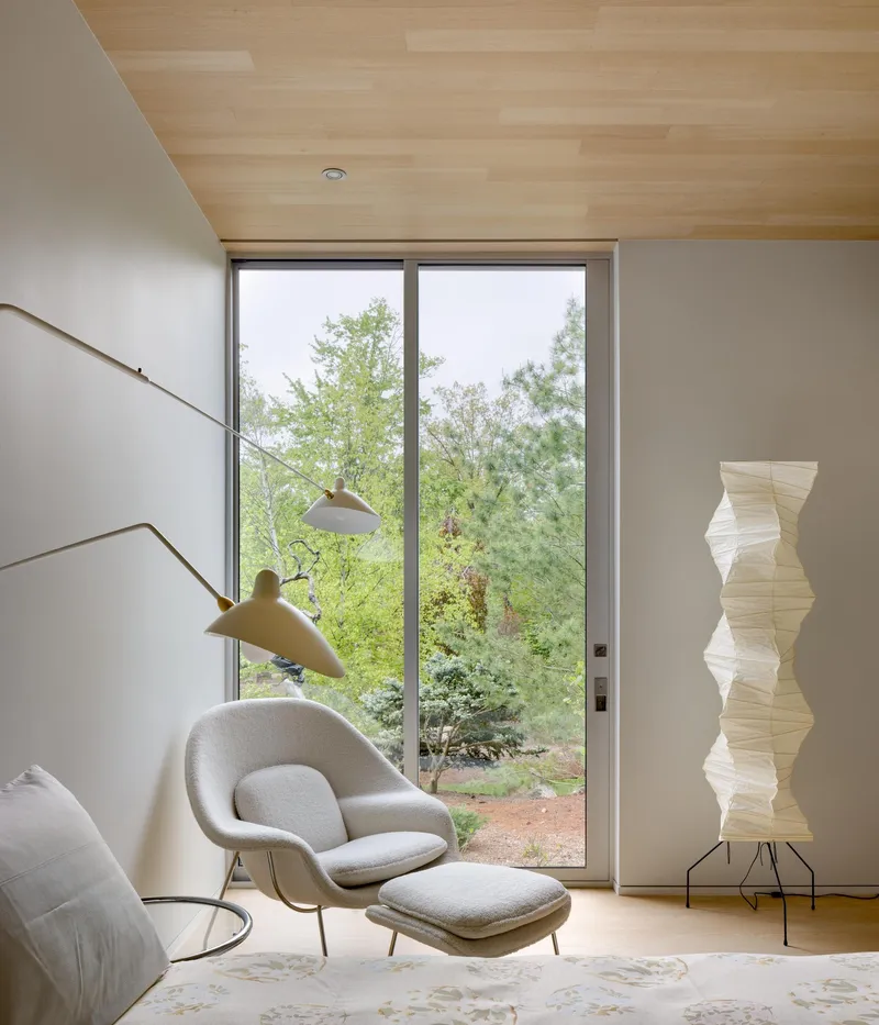 Seating area with floor-to-ceiling window overlooking garden and wood ceiling plane above white walls