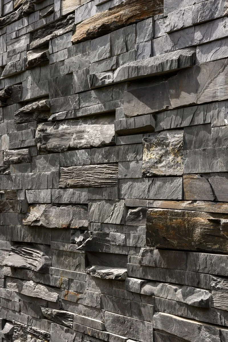 Close-up of stacked slate cladding with rough-hewn edges and varied grey and brown tones in natural light