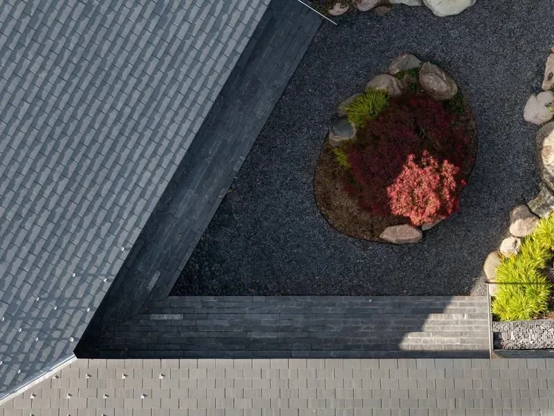 Aerial view of slate roof corner meeting gravel courtyard with planted bed containing red foliage and boulders