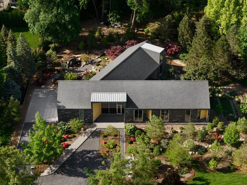 Aerial view of the gabled roof and black timber facade surrounded by planted garden beds
