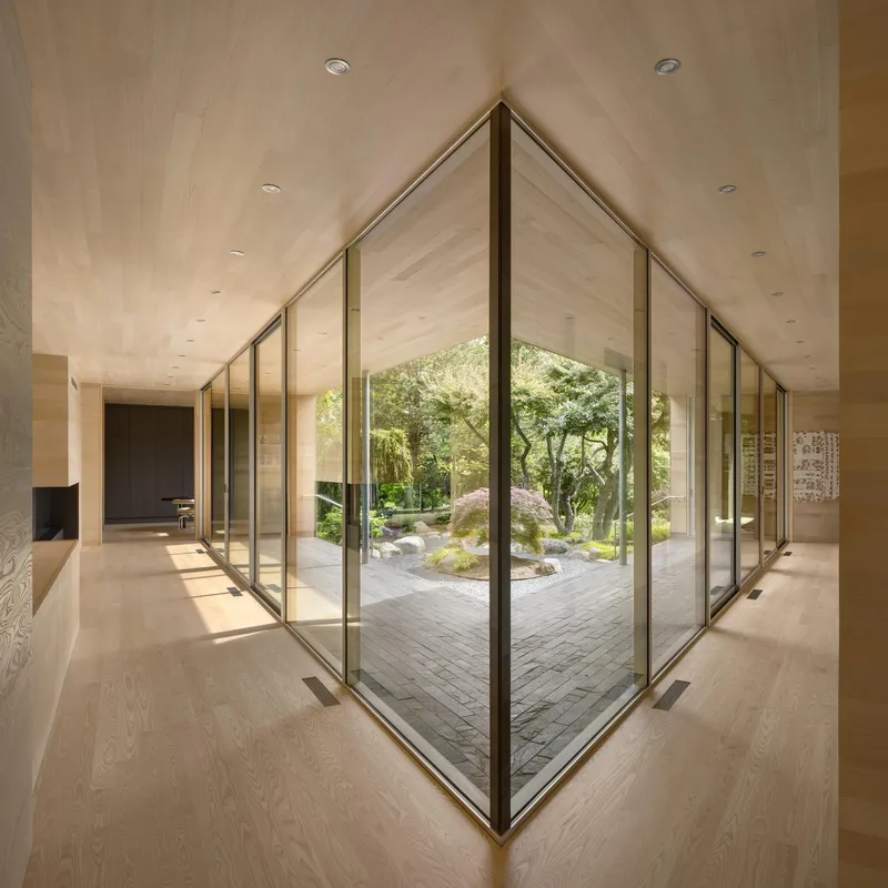 Corner glass walls framing an interior courtyard with brick paving and moss under dappled light
