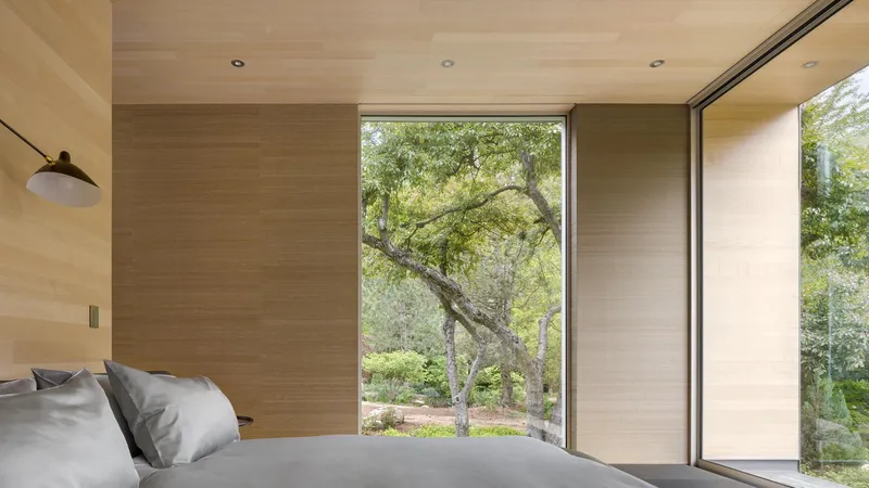 Bedroom with plywood wall panels and sliding glass doors opening to trees outside