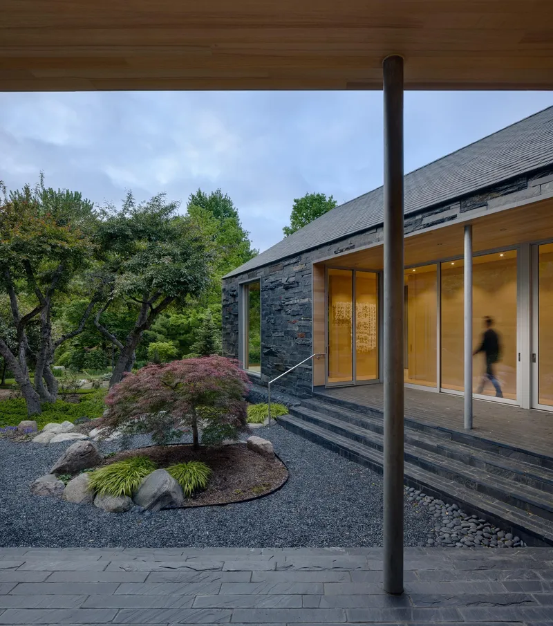 Covered entry terrace with planted bed featuring Japanese maple and grasses beside glass doors at dusk