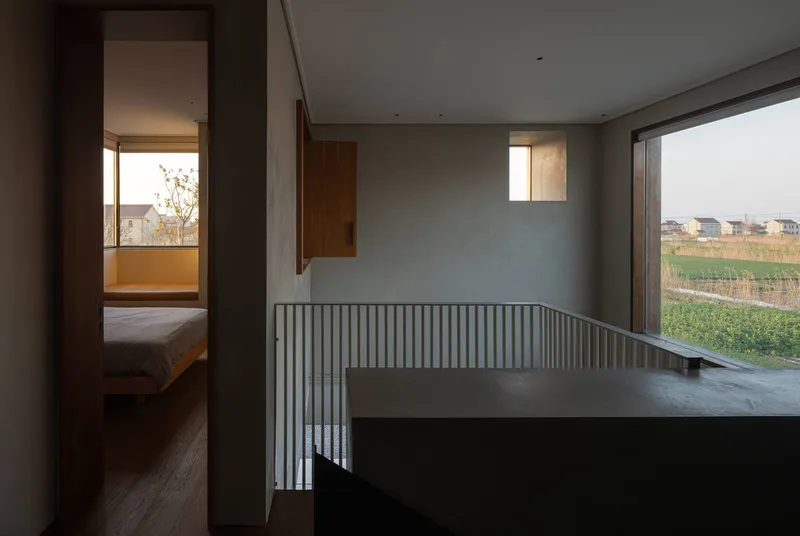 Upper landing with vertical slat railing opening to bedroom and large windows framing rural landscape
