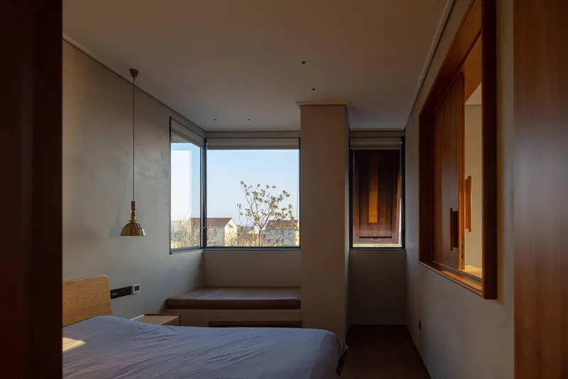 Bedroom with corner windows, timber built-in desk and pendant light in afternoon sun
