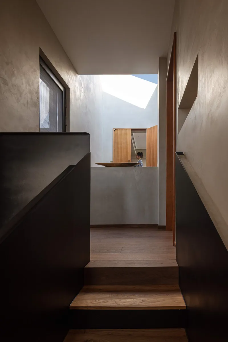 Stair landing with black metal balustrade and angled skylight casting geometric shadow on plaster walls