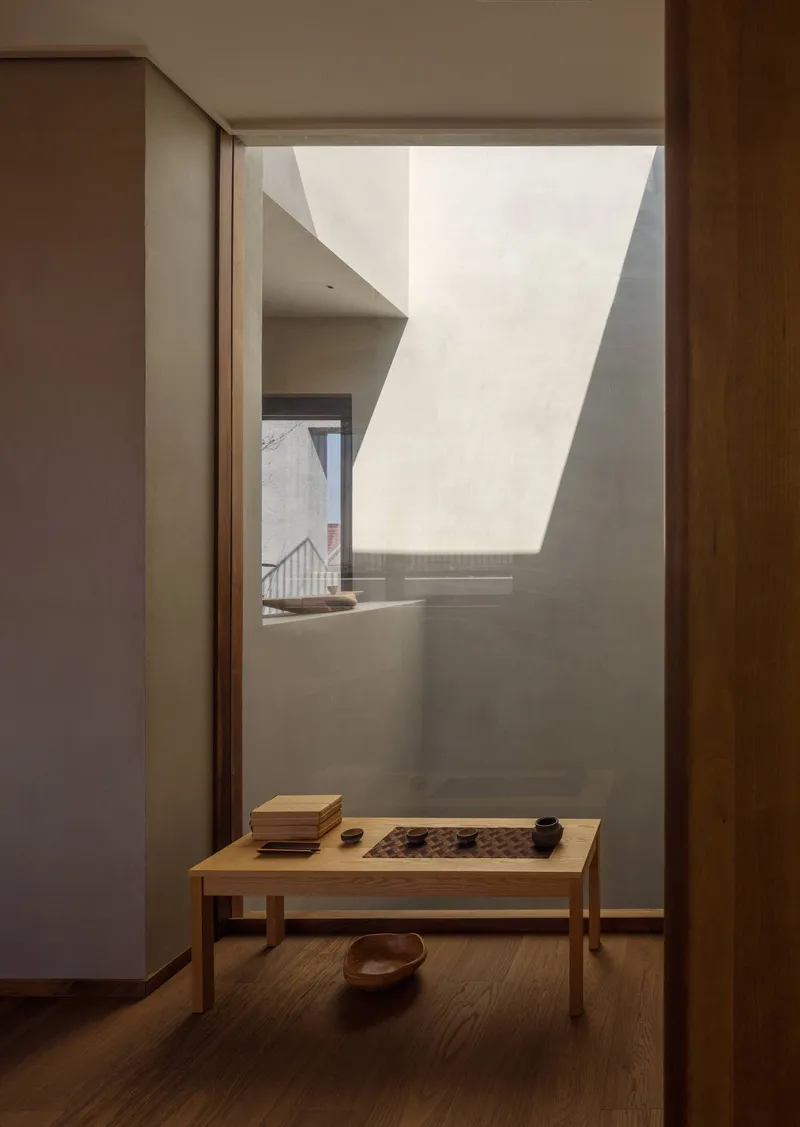 Low timber table beneath an angular skylight washing the white plaster wall with daylight