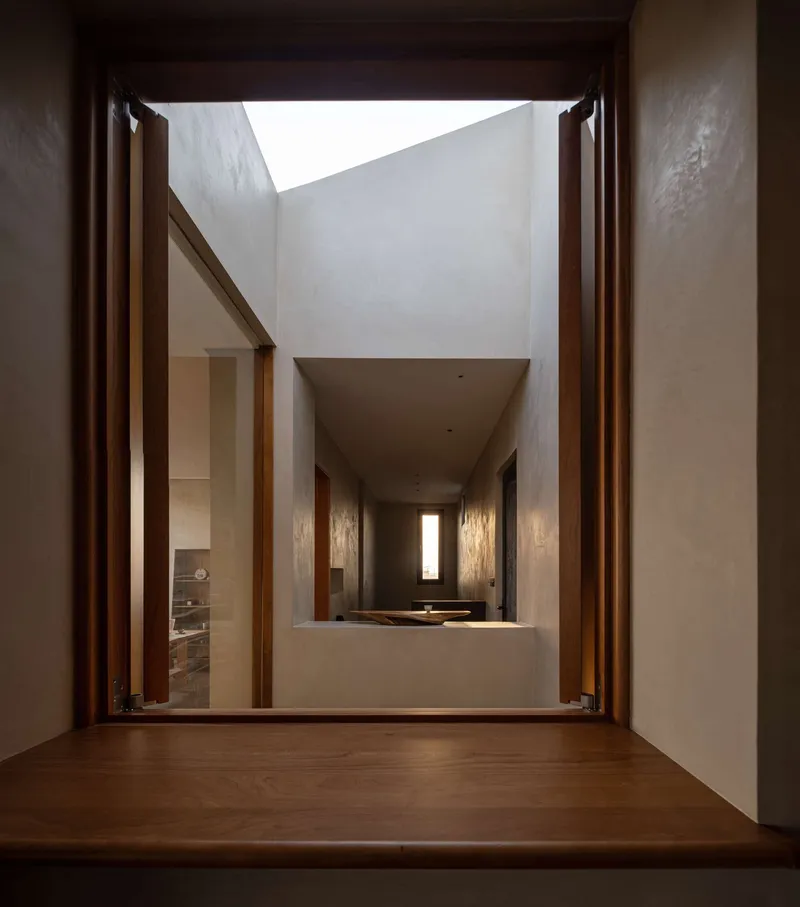 Timber-framed doorway opening to a double-height courtyard with white plastered walls and clerestory skylight