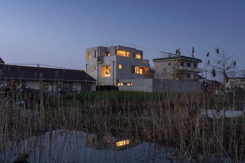 Rear elevation reflected in the wetland pond at dusk with illuminated interior windows