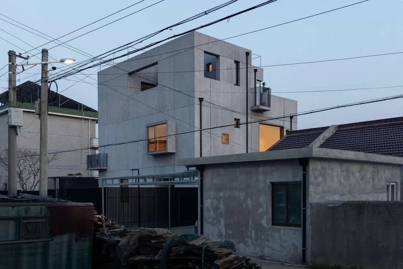 Gray concrete block facade with scattered square windows and overhead power lines at twilight