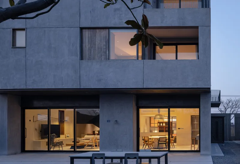 Close view of the stacked volumes with timber shutters and glazing framed by bare tree branches