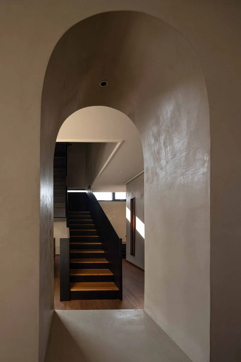 Arched passageway framing the black steel staircase with timber treads and afternoon light from above