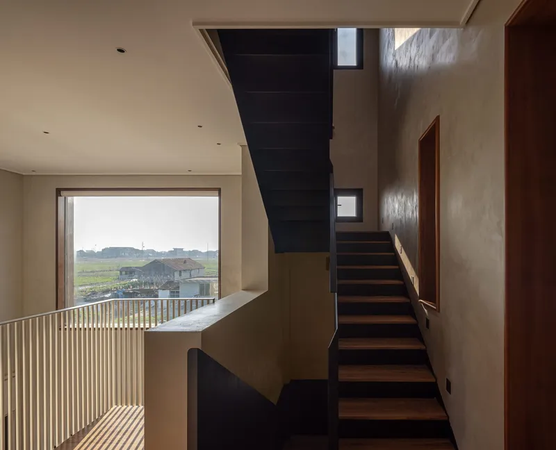 Angled staircase with dark metal stringers and timber treads beside a vertical slot window overlooking farmland