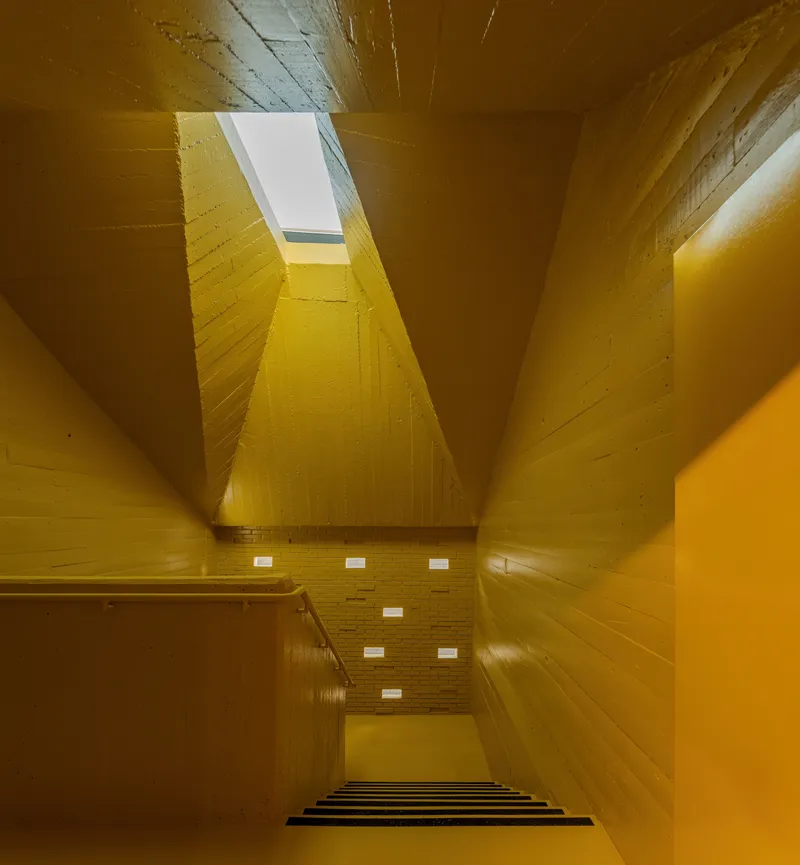 Looking up through a yellow-painted timber stairwell with a rectangular skylight at the top