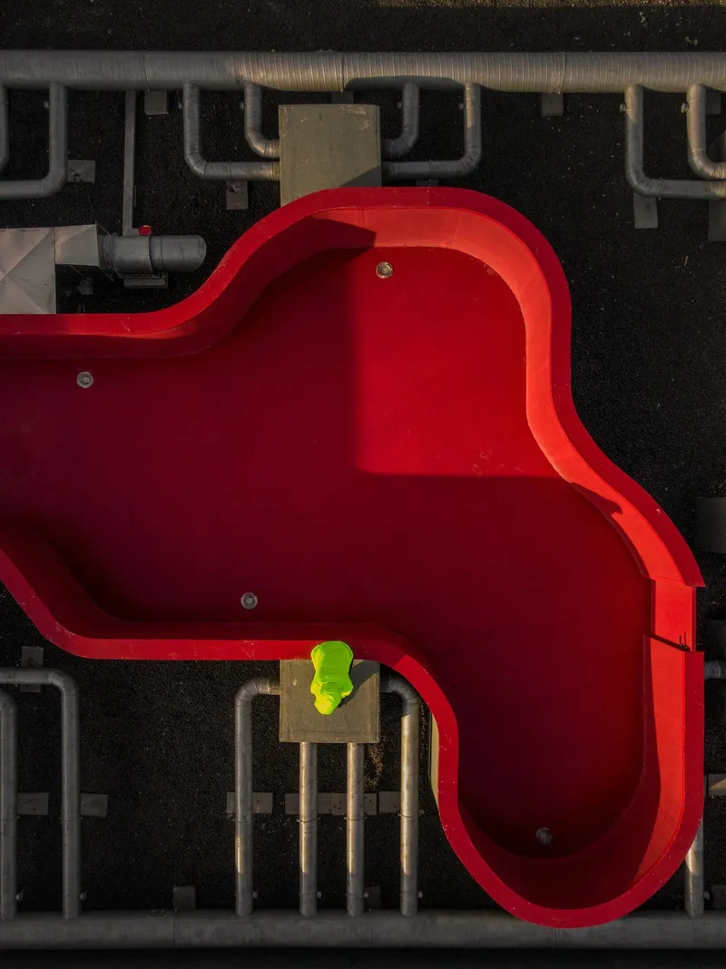 Drone view of the red curving rooftop pool with a worker in fluorescent yellow standing inside