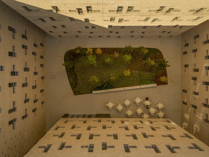 Aerial view into a courtyard with a vegetated wall, patterned paving, and small white tables below