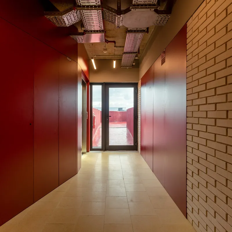 Corridor with maroon wall panels and exposed ceiling ducts leading to a glazed door