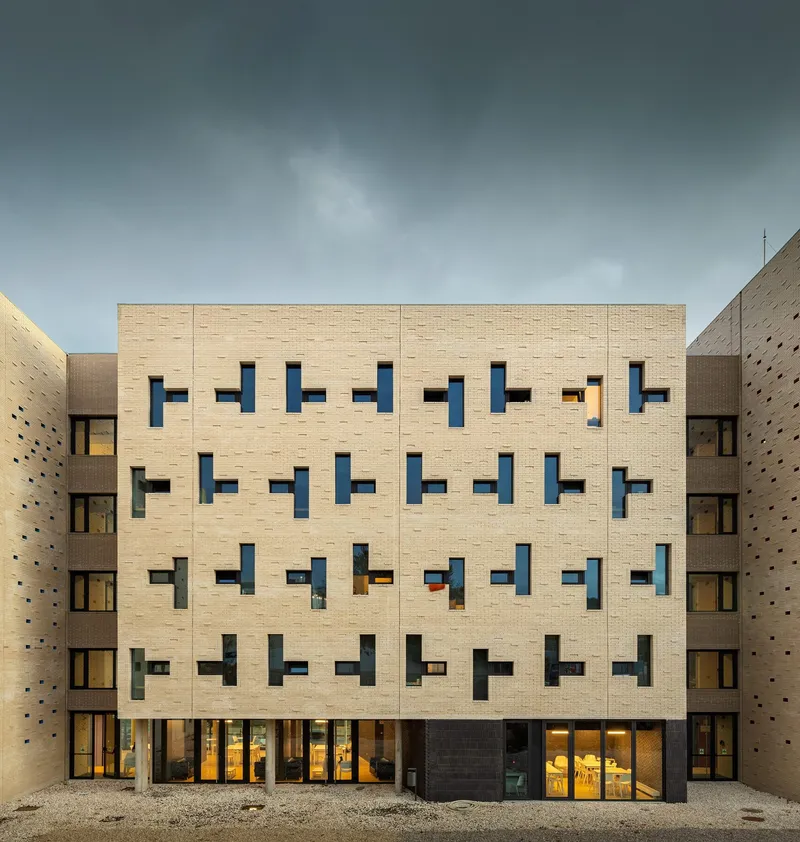 Courtyard facade with buff brick and irregular window openings under overcast skies