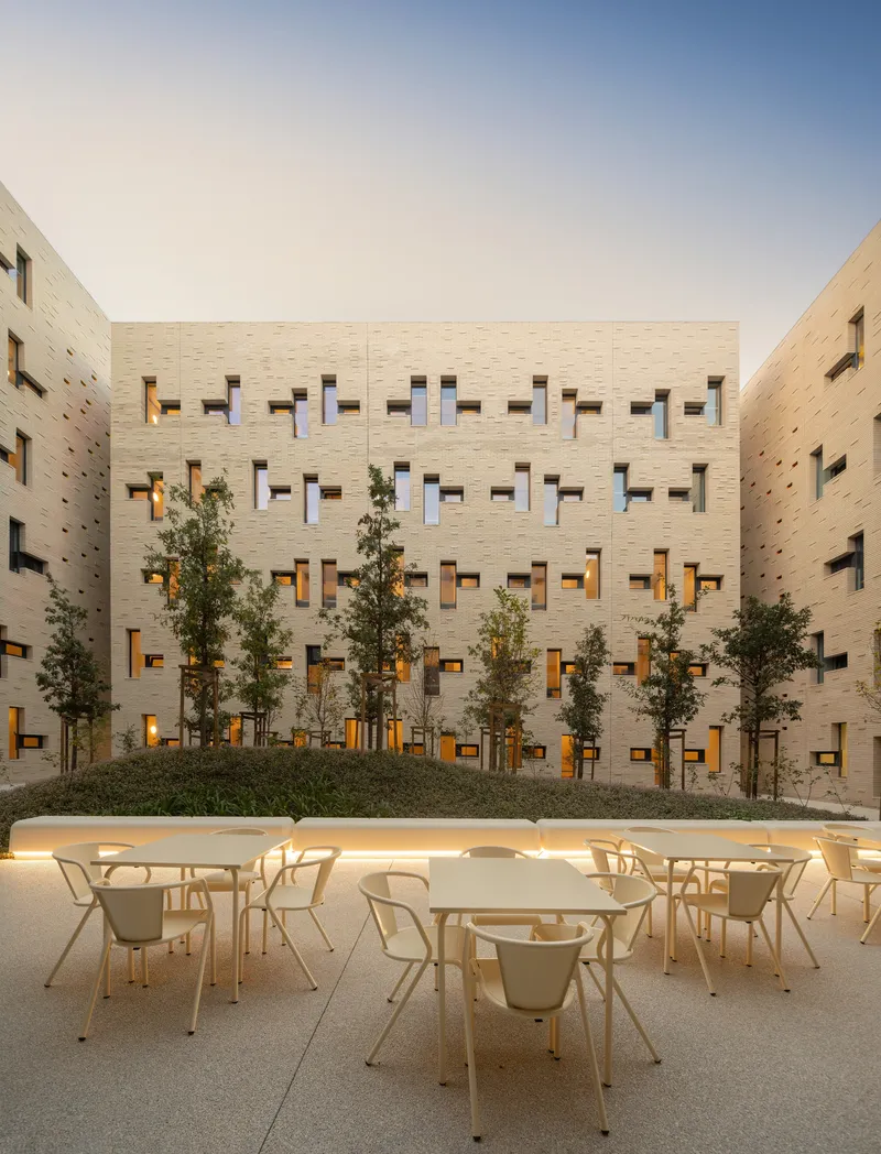 Outdoor seating area with tables and chairs facing planted trees at dusk