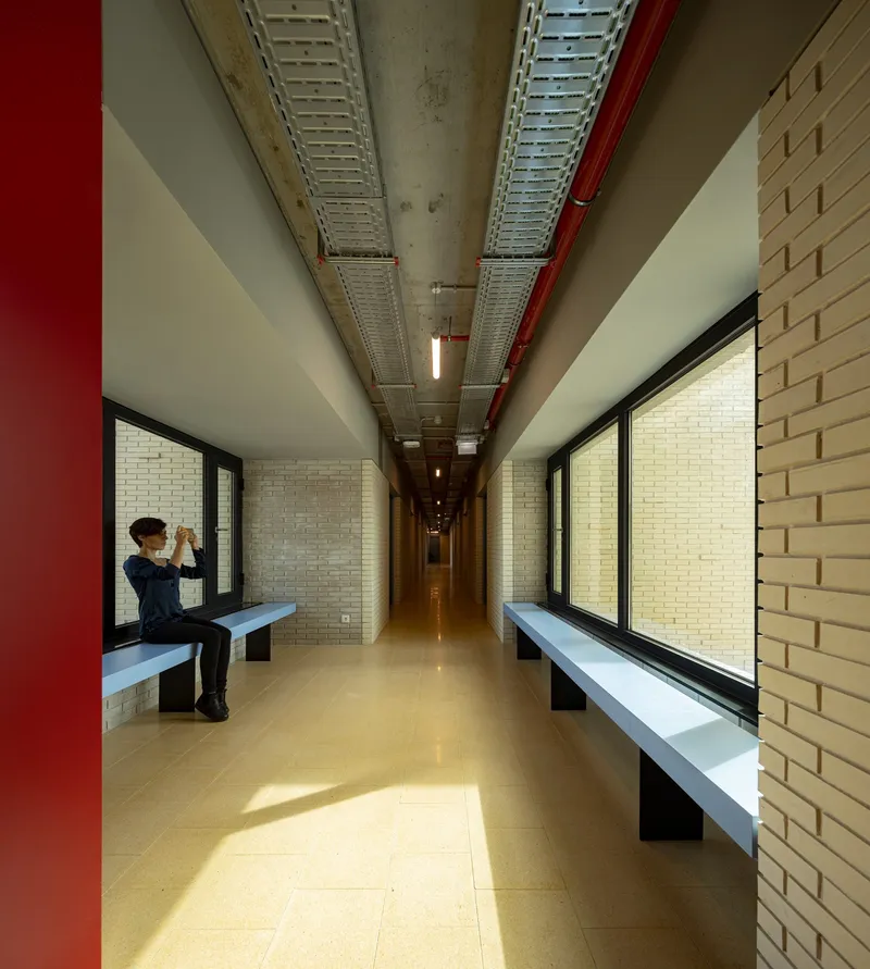 Long corridor with brick walls, bench seating, and exposed ceiling ducts with a seated figure