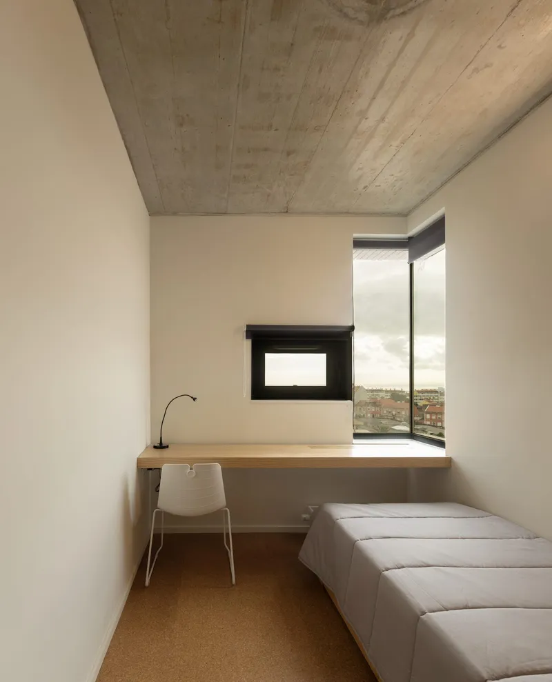 Bedroom with corner window, timber desk, board-formed concrete ceiling and cork flooring
