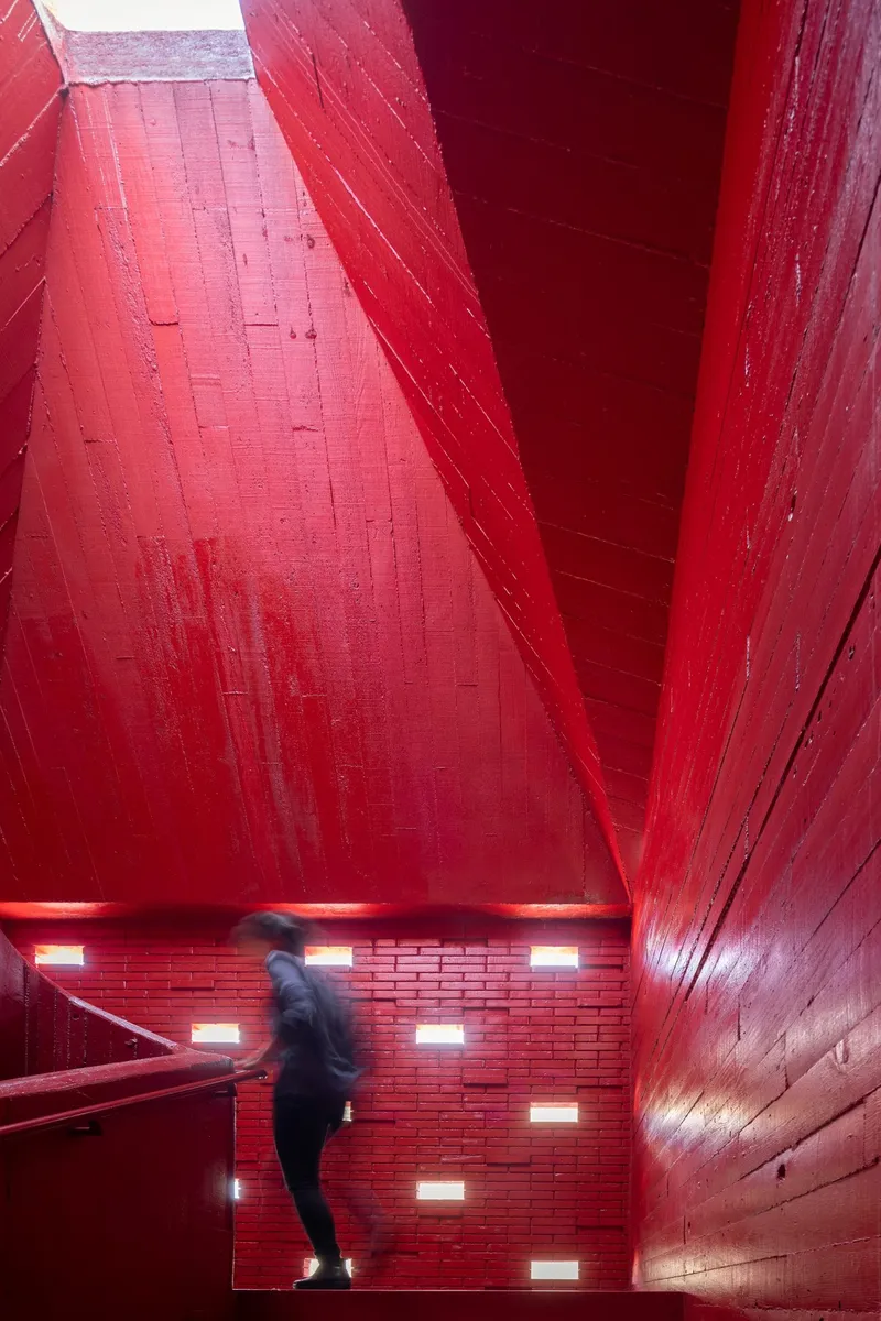 Stairwell clad entirely in red-painted timber with a descending figure