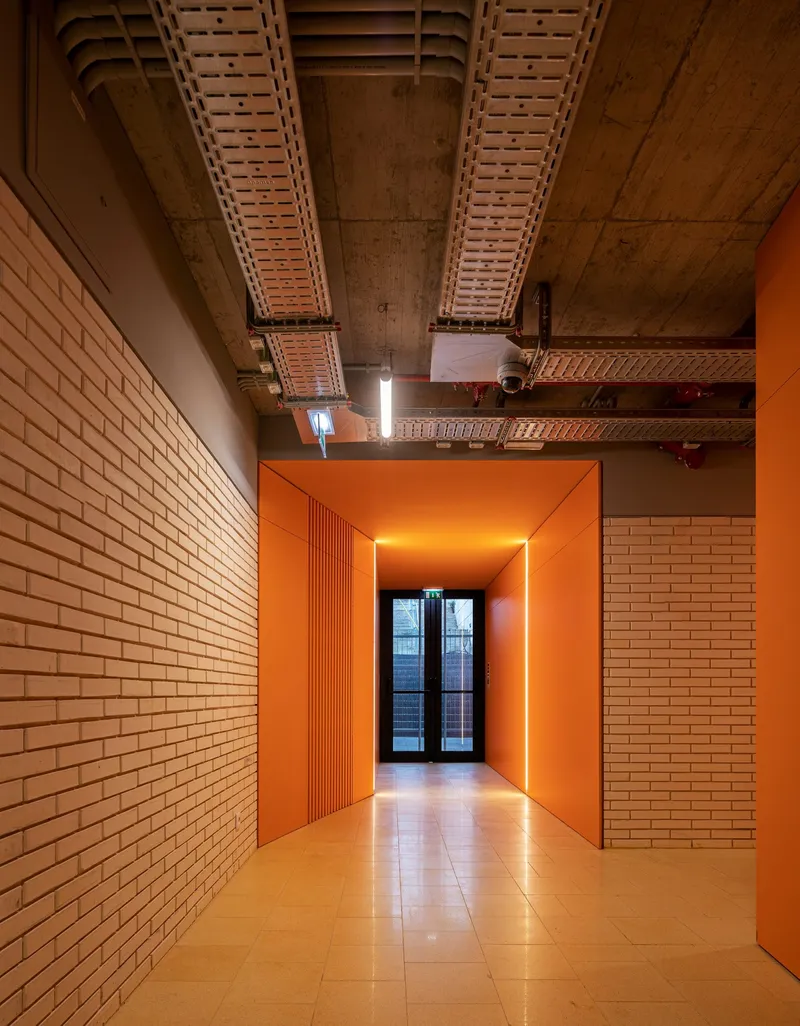 Orange painted corridor framed by cream brick walls with exposed concrete ceiling and terracotta panels