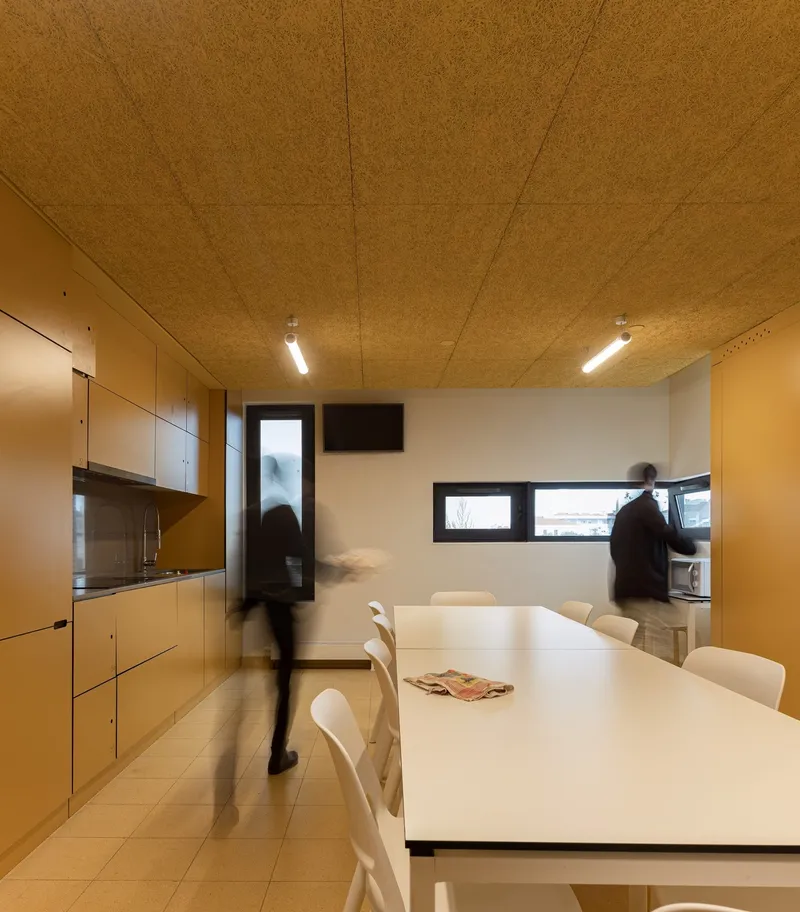 Communal kitchen and dining area with cork ceiling panels and people in motion blur