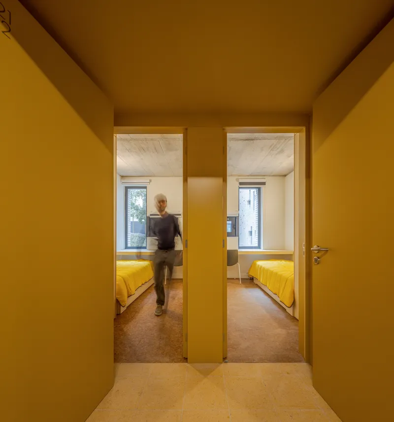 Mustard hallway looking through two doorways into bedrooms with yellow bedding and a person passing through