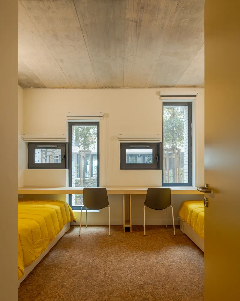 Double bedroom with yellow beds beneath stacked windows and exposed concrete ceiling vault