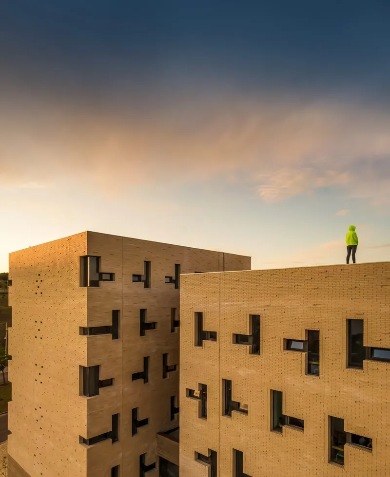 Brick facade with staggered window openings and a worker in high-visibility vest on the roof at dusk