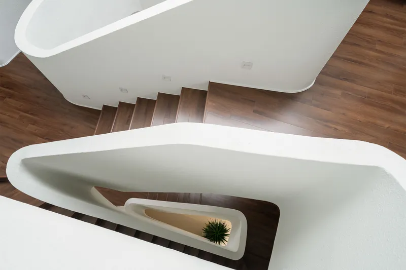 Top-down view of curving white staircase with timber treads and recessed planter holding small plant