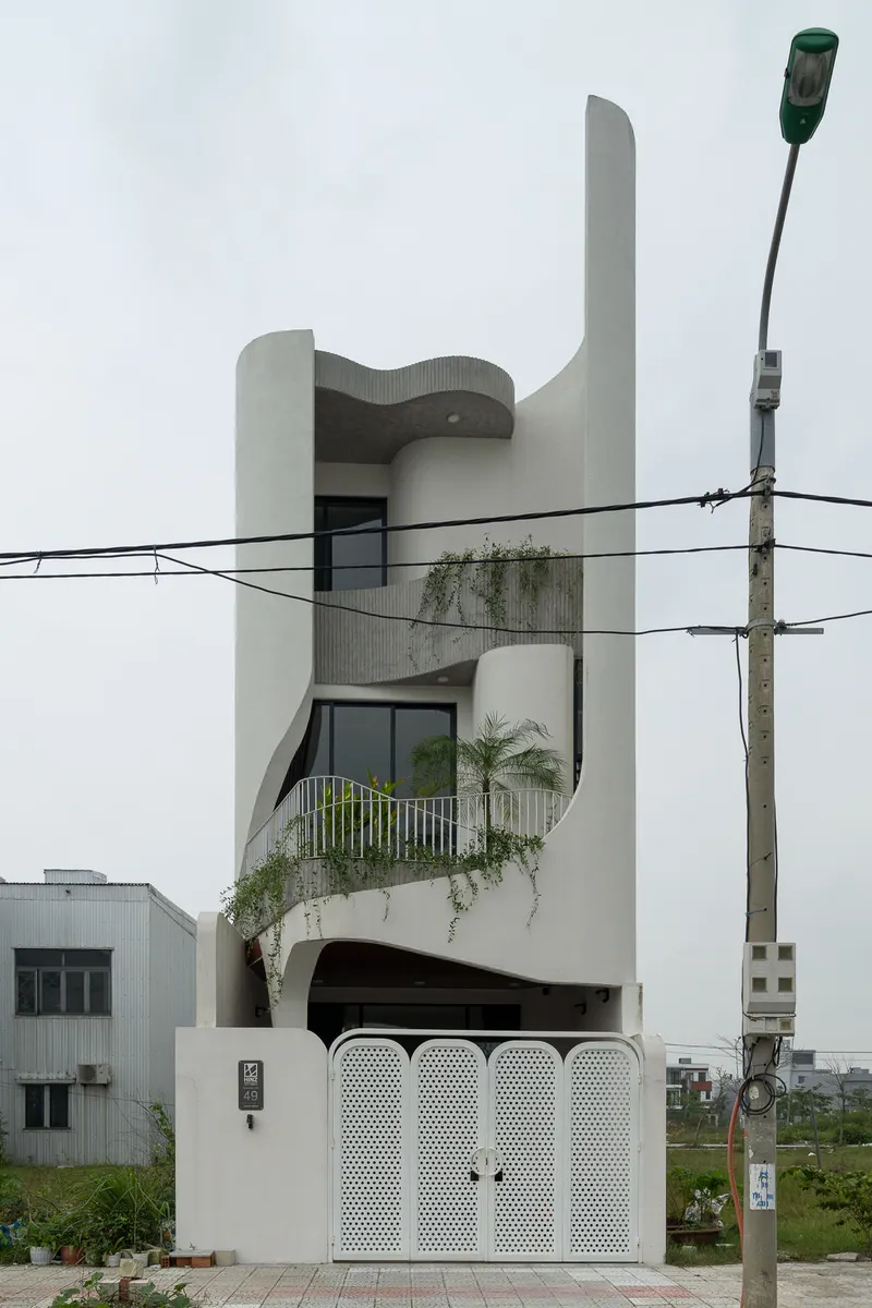 Street view of the white sculptural facade with curved balconies, planted terraces and perforated gate panels
