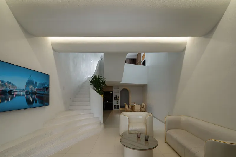 Double-height living space with curved white staircase, recessed ceiling lighting and upholstered seating
