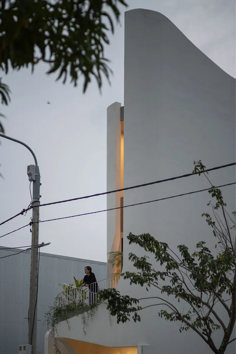 Dusk view of the white facade with illuminated vertical slot and figure on balcony