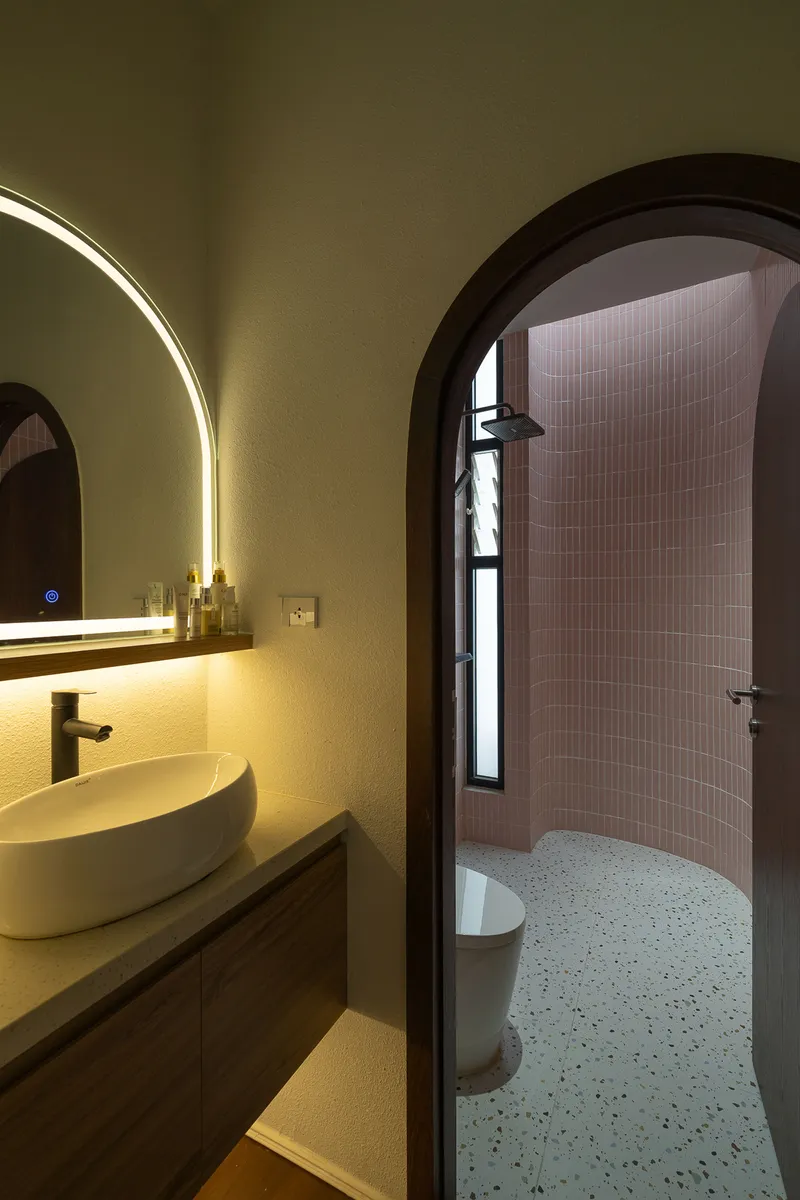 Arched bathroom entry revealing pink tiled shower enclosure and backlit circular mirror above vessel sink