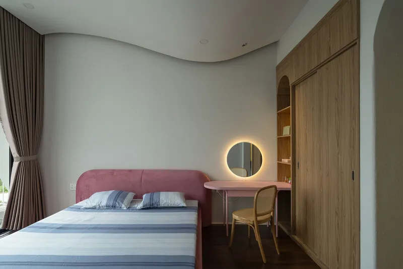 Bedroom with pink upholstered bed and integrated timber desk beneath curtained window in soft daylight