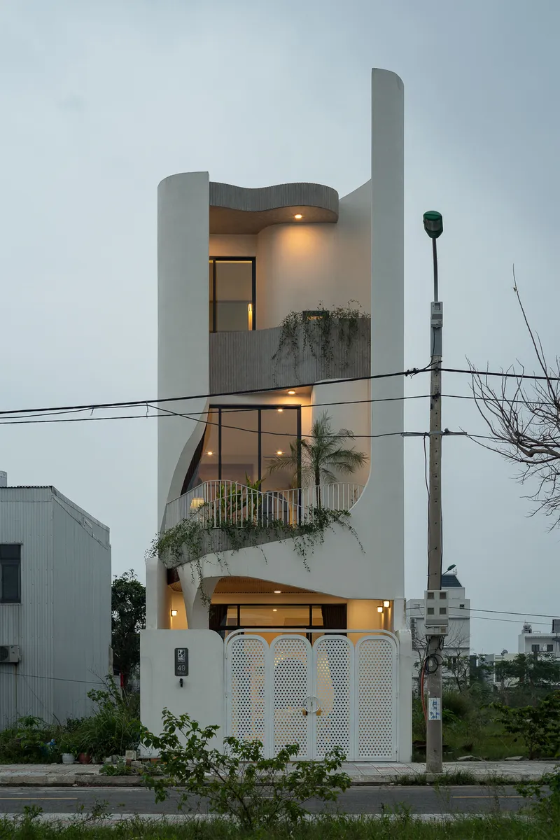 Three-storey white facade with curved parapet and planted balconies at dusk under power lines