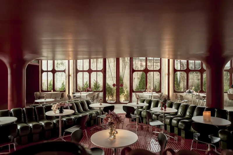 Restaurant dining area with tufted banquette seating and rounded steel columns beneath arched windows overlooking greenery